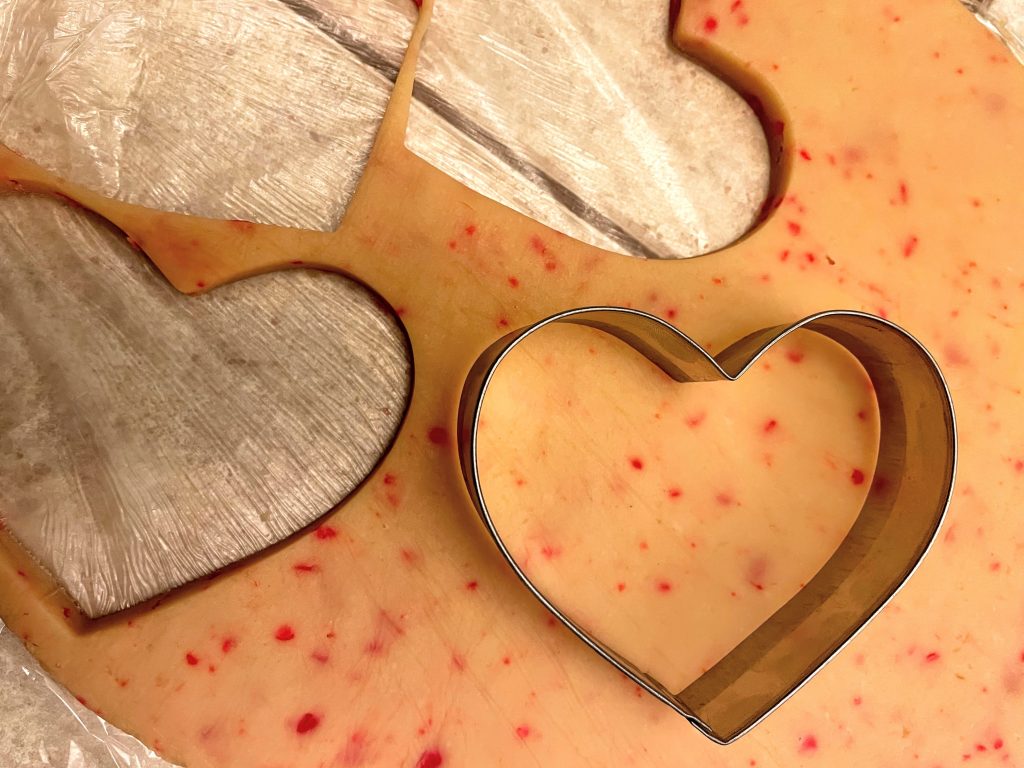 Red Hot Sugar Cookie dough rolled out and being cut with a metal heart shaped cutter